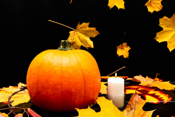 Pomerančová dýně hořící svíčku na stole se žlutými a červenými javorovými listy. Halloween, teplá podzimní atmosféra.Tmavě černé pozadí s javorovými listy. - Fotografie, Obrázek