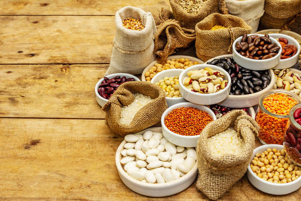 Assorted different types of beans and cereals grains. Set of indispensable sources of protein for a healthy lifestyle. Old wooden boards background, copy space - Photo, Image