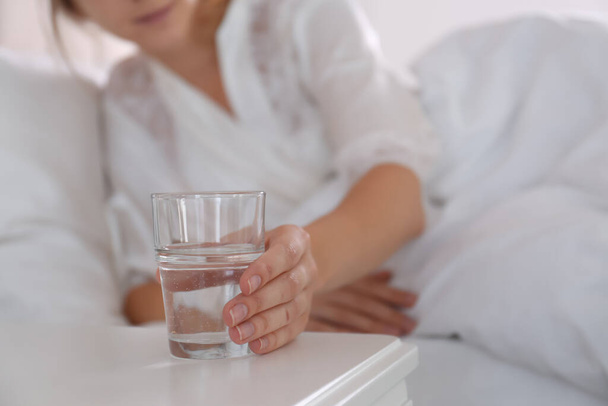 Woman taking glass of water from nightstand in bedroom, closeup - Foto, Imagem