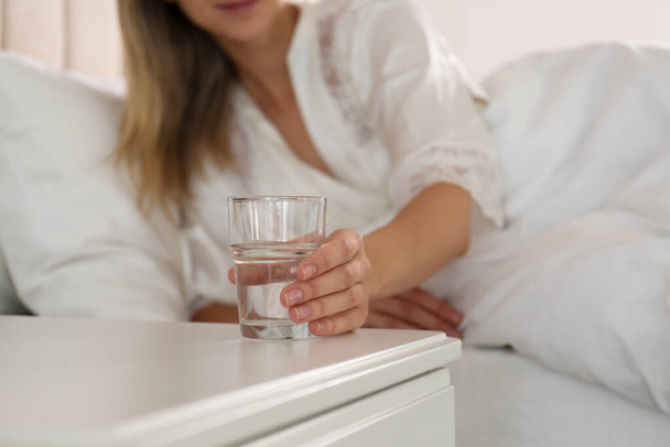 Woman taking glass of water from nightstand in bedroom, closeup - 写真・画像