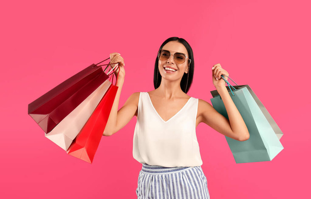 Beautiful young woman with paper shopping bags on pink background - Фото, зображення