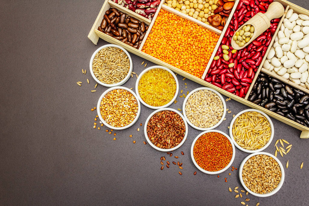 Vari tipi assortiti di fagioli e cereali. Set di fonti indispensabili di proteine per uno stile di vita sano. Pietra nera sfondo di cemento, vista dall'alto - Foto, immagini