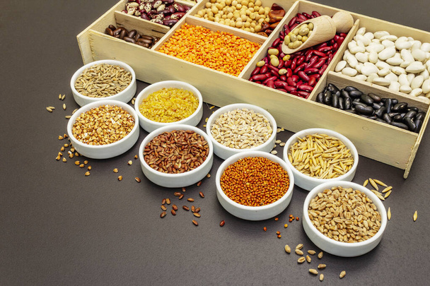 Různé druhy fazolí a obilných zrn. Sada nepostradatelných zdrojů bílkovin pro zdravý životní styl. Černý kámen betonové pozadí, kopírovací prostor - Fotografie, Obrázek