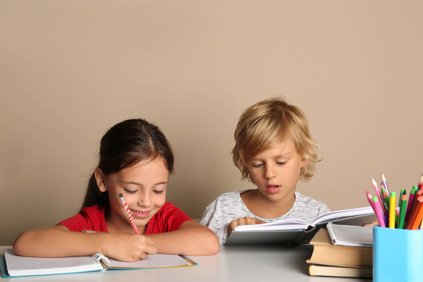Little boy and girl doing homework at table on beige background - Φωτογραφία, εικόνα