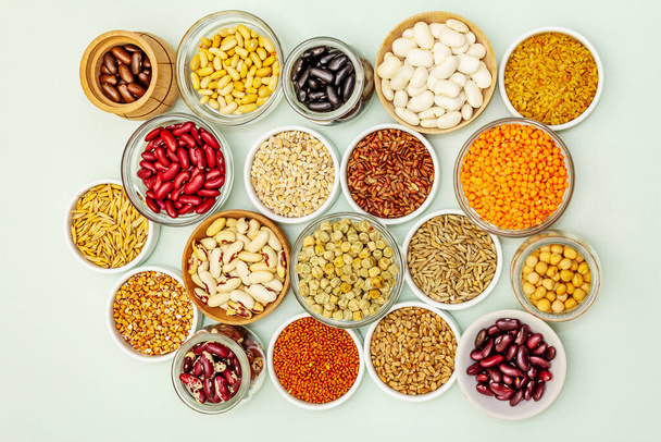 Různé druhy fazolí a obilných zrn. Sada nepostradatelných zdrojů bílkovin pro zdravý životní styl. Světle zelené pozadí, horní pohled - Fotografie, Obrázek