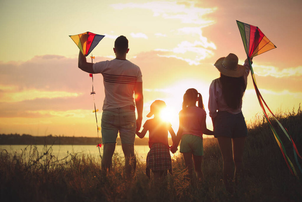 Parents and their children playing with kites outdoors at sunset, back view. Spending time in nature - Photo, Image