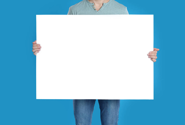 Man holding blank poster on blue background, closeup - 写真・画像