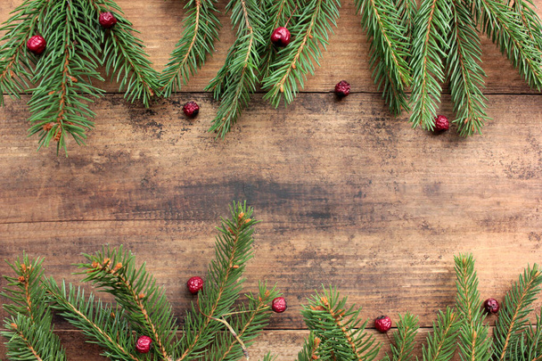 Fondo navideño con ramas de abeto y bayas rojas. Marco de vacaciones de invierno con ramas evegreen en mesa de madera. Colocación plana, espacio de copia - Foto, imagen