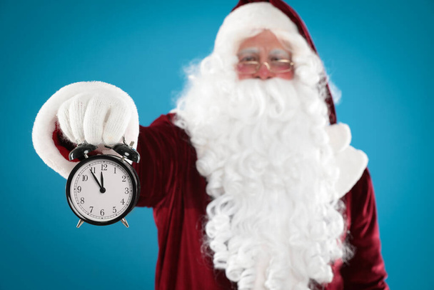 Santa Claus holding alarm clock on blue background, focus on hand. Christmas countdown - Foto, Imagem