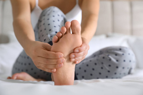 Young woman suffering from pain in foot on bed, closeup - Φωτογραφία, εικόνα