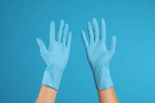 Doctor wearing medical gloves on light blue background, closeup - Foto, imagen