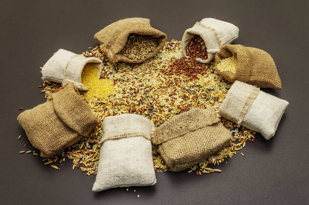 Diverse soorten granen in handgemaakte zakken. Meng van onmisbare ingrediënten voor een gezond dieet. Zwarte steen beton achtergrond, close up - Foto, afbeelding