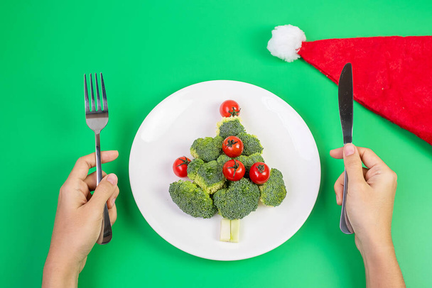 Arbre de Noël de légumes bio sur assiette blanche ; Brocolis et tomates avec fourchette et couteau sur fond vert. Joyeux Noël et bonne fête de nouvelle année, New You, Alimentation saine et concept végétarien - Photo, image