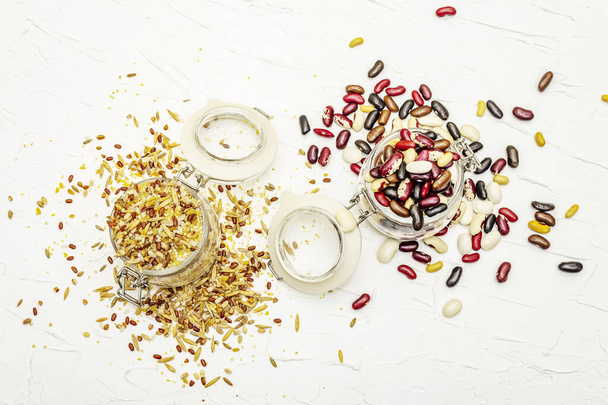 ガラス瓶に穀物や豆の様々なミックス。健康な生活のためのタンパク質の不可欠な源のセット。白いパテの背景、トップビュー - 写真・画像