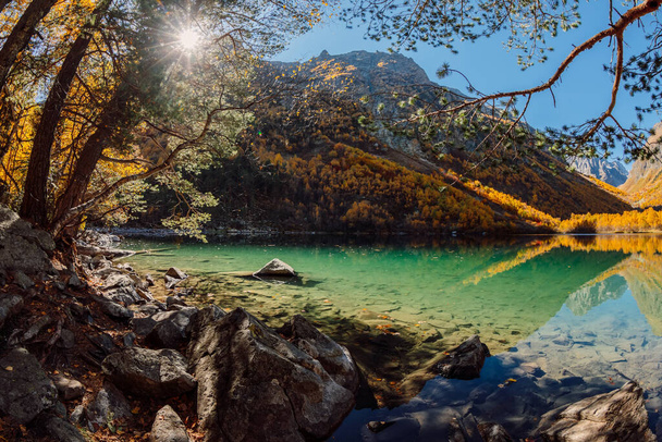 Ορεινή λίμνη με διάφανο νερό και πολύχρωμα φθινοπωρινά δέντρα. Βουνά και λίμνη - Φωτογραφία, εικόνα