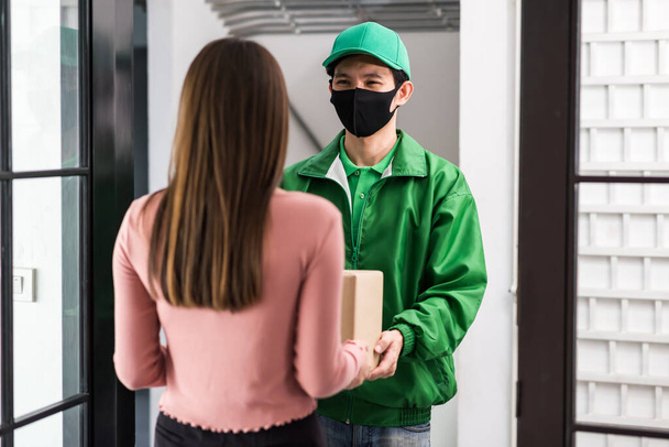 Rear of office woman receiving parcel from Asian courier deliveryman in uniform and face mask at door entrance. New normal to shopping by mobie phone application during covid19. - Fotoğraf, Görsel