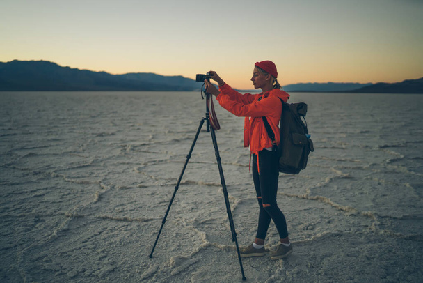 Full body of female traveler with backpack standing on rough surface of dead lake and preparing to take pictures on camera - Photo, image