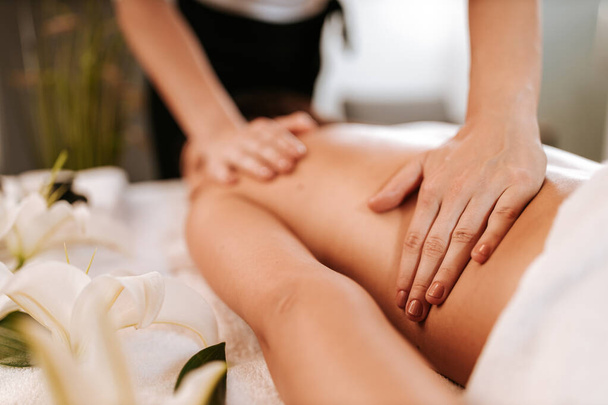 Koncepcja zabiegu kosmetycznego z masażystą i jej pacjentem. Masażysta robi masaż kobiecego ciała w salonie spa. Piękna dziewczyna z brązowymi kręconymi włosami i kreolską skórą o regeneracji masażu. - Zdjęcie, obraz