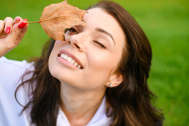 Bella ragazza bruna guardare il cielo attraverso asciutto acero autunno foglia a verde parco sfondo, godere di stagione autunnale all'aperto - Foto, immagini