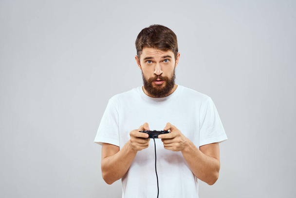 Mies, jolla on peliohjain käsissään pelaamassa pelejä vapaa-ajan elämäntapa tekniikka valkoinen t-paita kevyt tausta - Valokuva, kuva