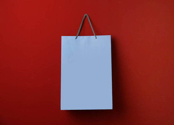Paper shopping bag hanging on red background - Фото, изображение