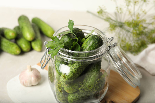 Pickling jar with fresh cucumbers on light table, closeup - Foto, afbeelding