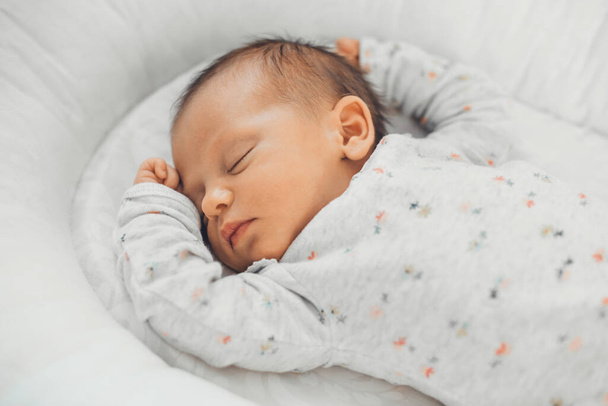 Foto von oben von einem kaukasischen Neugeborenen, das in weißer Kleidung zu Hause schläft - Foto, Bild