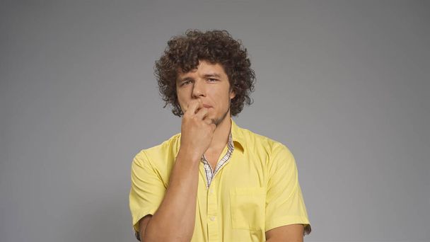 Pensive young man doubts covering his mouth with hand. Cut out on gray background - Foto, imagen