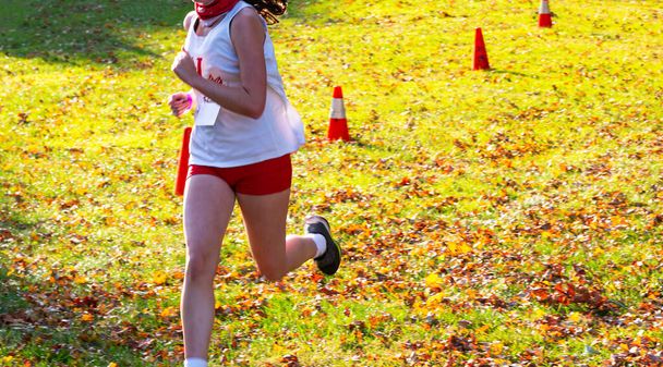 Frontansicht eines Highschool-Mädchens Cross-Country-Läuferin läuft ein Rennen auf Gras und verlässt im Herbst. - Foto, Bild