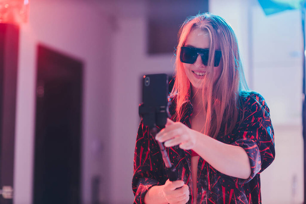 Atractiva mujer joven en camisa a cuadros tomando selfie usando monópodo con teléfono inteligente. - Foto, imagen