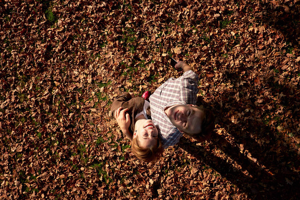 Šťastný atraktivní pár objímání a úsměv na kameru při chůzi v podzimním parku - Fotografie, Obrázek