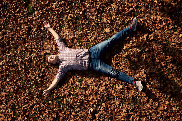 Onnellinen nuori, viehättävä mies suljetuin silmin makaa maassa syksyllä puistossa ja rentouttava. - Valokuva, kuva