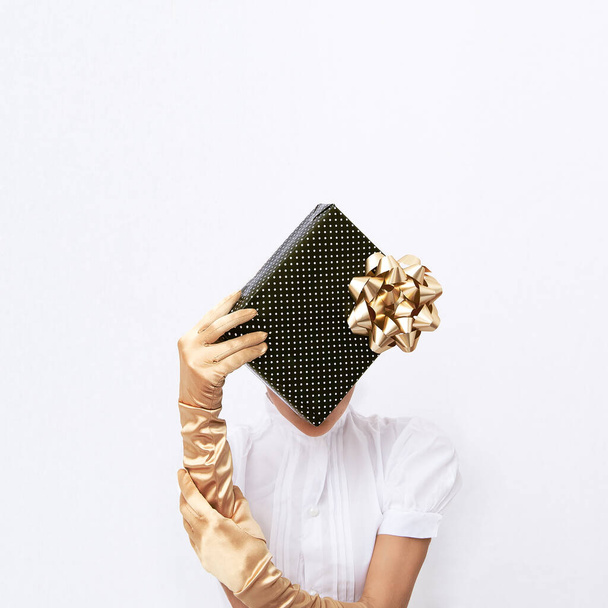 Γυναίκα σε χρυσά ρετρό γάντια κρατήσει κουτί δώρου. Polka τελείες διακόσμηση σε λευκό φόντο χώρο. Minimal fashion εορταστικά Χριστούγεννα / Πρωτοχρονιά, γιορτές, πάρτι γενεθλίων, εορταστική έννοια. - Φωτογραφία, εικόνα