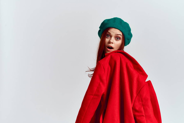 A woman holds in her hand a red coat and a dark T-shirt Green hat cropped view of a light background - Foto, imagen