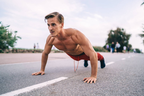 Strong Caucasian sportsman with muscular body shape doing push ups on street enjoying morning workout training, strength shirtless male athlete keeping vitality and wellness on intensive activity - Fotografie, Obrázek
