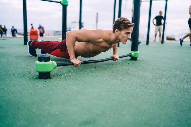 Experienced Caucasian guy enjoying morning workout doing push up plank for training arms, muscular sportsman have endurance exercising on sports ground for keeping perfect body physical shape - Фото, изображение