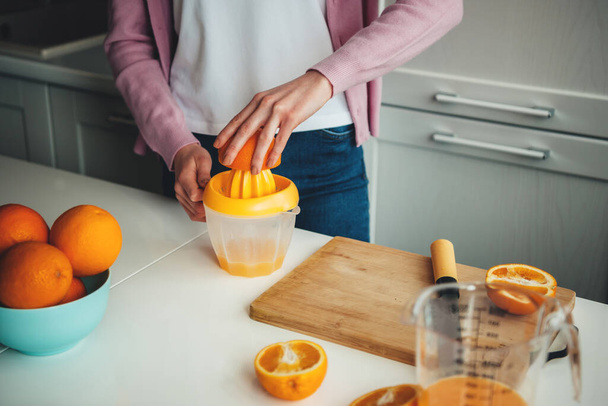 Close up foto de uma mulher caucasiana espremendo suco fresco de laranjas fatiadas na cozinha - Foto, Imagem