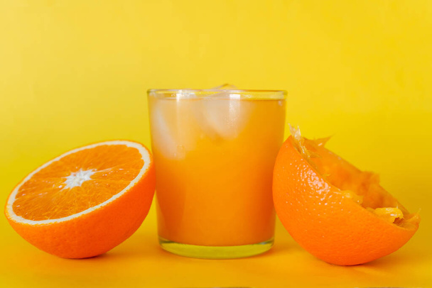 Verfrissend glas sinaasappelsap met ijs en een sinaasappel in tweeën gesneden aan de zijkant. Levendige gele achtergrond.  - Foto, afbeelding