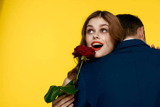 amantes hombre y mujer con una rosa roja en sus manos abrazándose en un fondo amarillo romance relación amor familia - Foto, Imagen