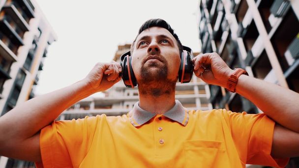 Man wearing safety equipment hearing protection. Worker wearing noise cancelling ear defenders or ear muffs. Construction builder puts on protect ears with headphones. Taking care safety during work. - Photo, Image
