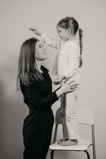 Een zwart-wit foto van een moeder die haar dochter knuffelt die op een barkruk staat. Een glimlachende moeder en kind zijn gelukkig. - Foto, afbeelding
