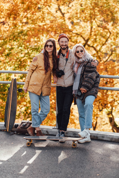 Kerl und zwei hübsche Mädchen posieren auf Brücke im Herbstpark - Foto, Bild
