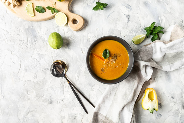 Σούπα καρότου από κοντά με φρέσκο καρότο, ψητές πιπεριές και τυρί, χυμό λάιμ και τζίντζερ, κουτάλι, σε ελαφρύ φόντο, πάνω όψη. - Φωτογραφία, εικόνα