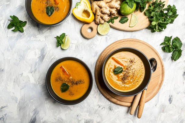 Fresh homemade cream of carrot soup with baked peppers, carrots and cheese, lime juice and ginger, served with nuts and fresh mint, place for text, top view. - Photo, Image