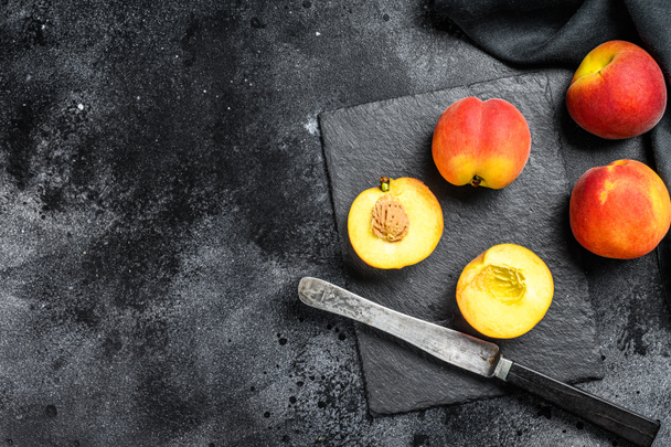 Organic Peaches fruit on a black stone Board. Black background. Top view. Copy space. - Foto, imagen