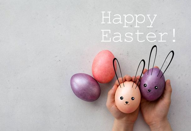 Easter card. Easter bunnies. Easter eggs painted in pastel colours, holded by kid's hands. Digital illustration. Text: Happy Easter. Copy space. Top view. Natural light. - 写真・画像