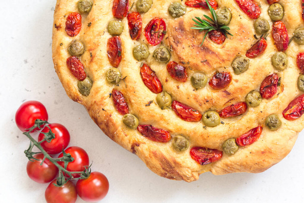 Homemade italian flat bread - Focaccia contorta. With olives, olive oil, rosemary, tomatoes. Traditional recipe. Vegan. White concrete texture background. - Photo, Image