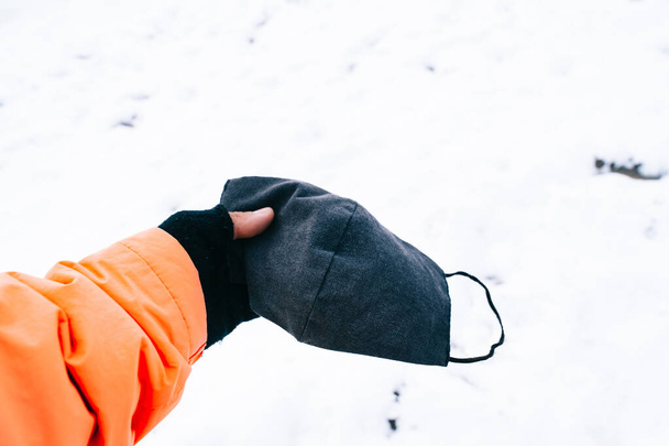 Hand met een medisch gezichtsmasker in de sneeuw. Concept van covid-19 pandemie in de winter van 2020. Gezichtsmasker in de sneeuw gebruiken. - Foto, afbeelding