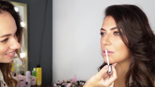 um artista de maquiagem está colorindo lábios com varinha de batom para a mulher elegância em uma jaqueta branca - Filmagem, Vídeo