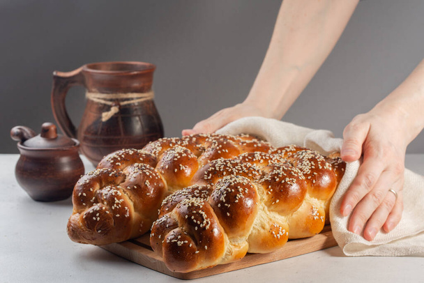 Frau mit frisch gebackenem Challah-Brot mit Mohn und Sesam. Bedeckt mit weißem Bezug. Auf weißem und grauem Hintergrund. - Foto, Bild